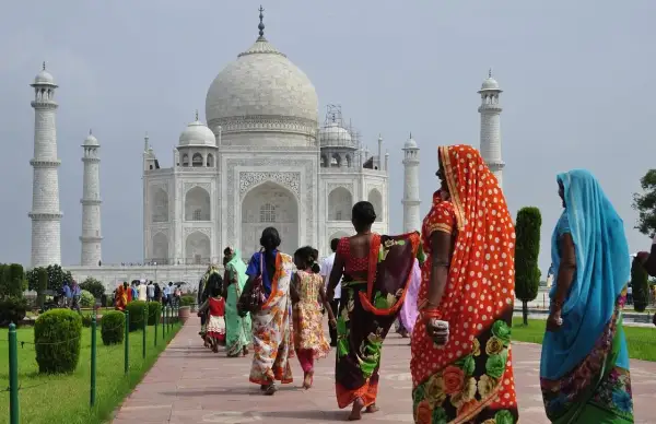 Kobiety w barwnych sari spacerują ścieżką ku Taj Mahal. Marzenie o podróży do Indii i uzyskaniu wizy do Indii staje się rzeczywistością.