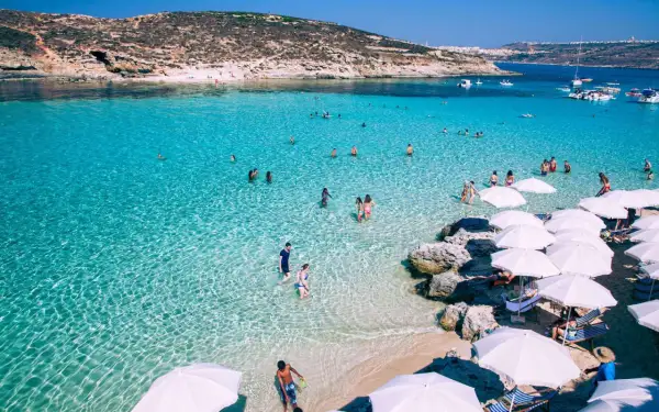 Malta w maju: turkusowa woda, plaża z białymi parasolami i ludzie kąpiący się w morzu.
