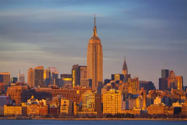 Zachód słońca nad Manhattanem. Widać Empire State Building i Chrysler Building. Zastanawiasz się, ile się leci do Nowego Jorku?