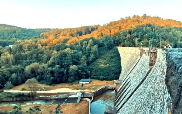 Kamienna zapora wodna w Zagórzu Śląskim otoczona zielonymi wzgórzami oświetlonymi zachodzącym słońcem.