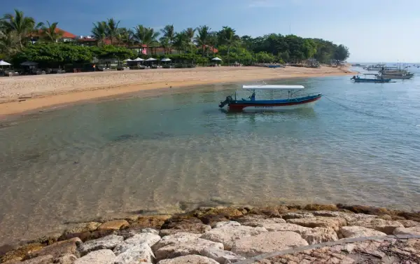 Spokojna plaża w Sanur z łodzią "Water Walk" kołyszącą się na turkusowej wodzie.