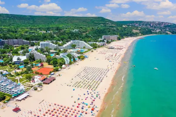 Słoneczna plaża na riwierze bułgarskiej pełna leżaków i parasoli, z turkusowym morzem i zielonymi wzgórzami w tle.