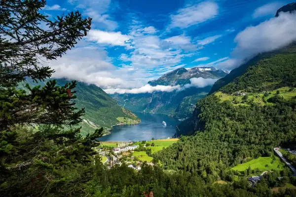 Widok na malownicze fiordy Norwegii, z górami porośniętymi lasem, jeziorem i statkiem wycieczkowym.