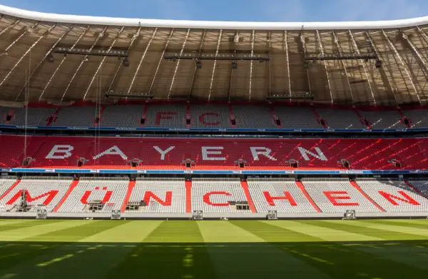 Puste trybuny Allianz Arena z napisem "BAYERN MÜNCHEN" w czerwonych i białych siedzeniach.