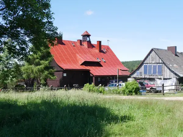 Urokliwa chatka gorzystow z czerwonym dachem, otoczona zielenią. Obok drewniany budynek z panelami słonecznymi.