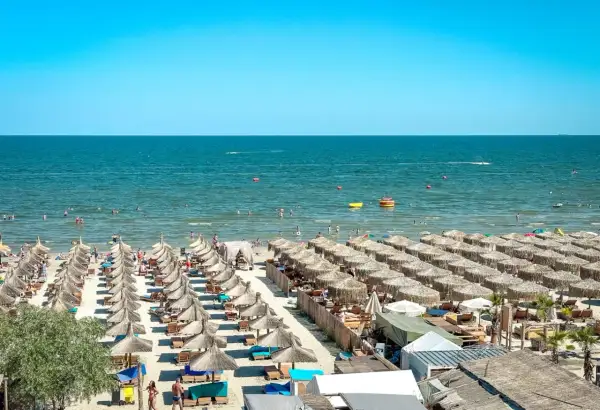 Słoneczny dzień na plaży nad Morzem Czarnym w Rumunii. Rzędy parasoli, ludzie kąpiący się i pływający.