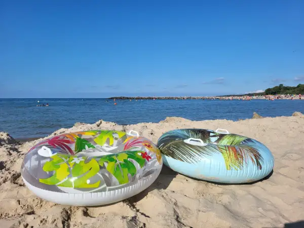 Dwa dmuchane koła na piaszczystej plaży, morze i tłumy ludzi w tle. Idealne na wakacje.pl opinie.