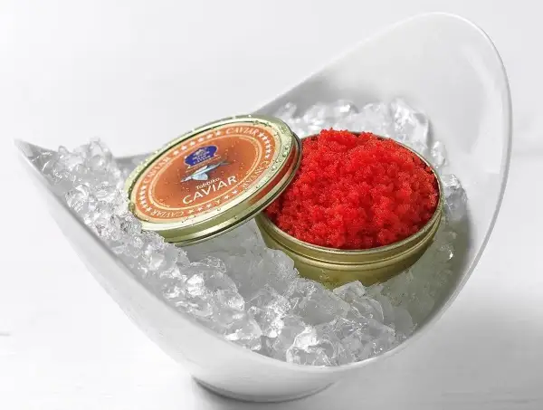 Czerwony kawior tobiko w puszce, podany na lodzie w białej misie.