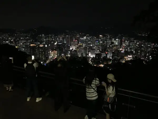 Nocny widok na rozświetlone miasto, przypominające panoramę Gangnam. Ludzie robią zdjęcia, podziwiając miejski krajobraz.