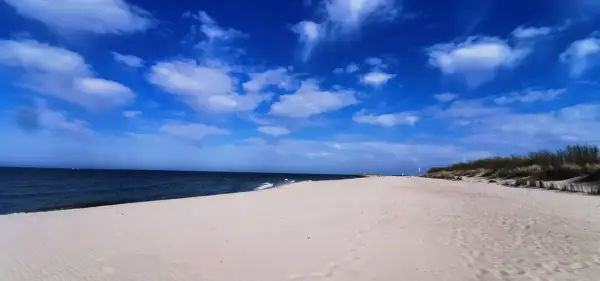 Piękna, słoneczna pogoda na sierpień nad morzem. Szeroka, piaszczysta plaża, spokojne morze i błękitne niebo z białymi chmurami.