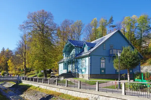 Piękny, błękitny budynek sanatorium Nida-Zdrój otoczony jesiennymi drzewami. Wiele pozytywnych **sanatorium Nida-Zdrój opinie** potwierdza urok tego miejsca.