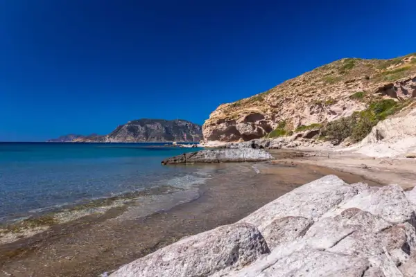 Majowa pogoda na Kos: skalista plaża z turkusową wodą i łagodnymi falami, w tle góry.