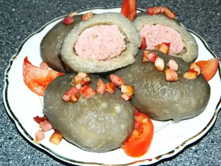 Cepelin z mięsem, polany skwarkami i podany z pomidorem. Wyglądają jak małe cepeliny na talerzu.
